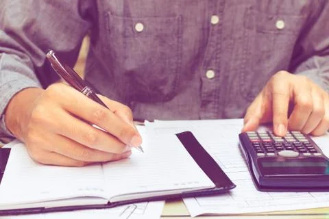 Man using calculator and writing note in home office. Stock Photos