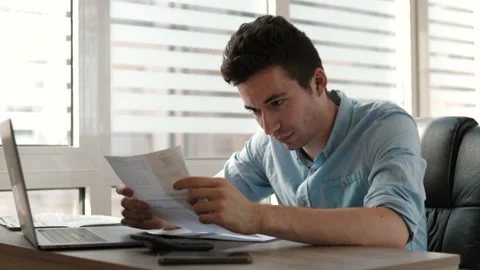 Man using calculator paying bill online holding paper sitting at  office desk. Stock Footage 202277516