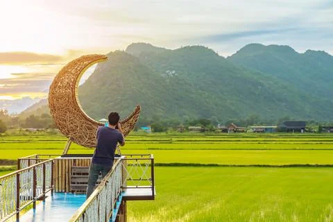 Man using camera to take photo with crescent moon chair made of rattan in p.. Foto stock