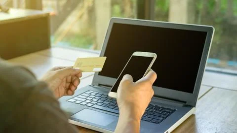 Man using a card, smartphone, and laptop on a desk, selective focus. Stock Photos