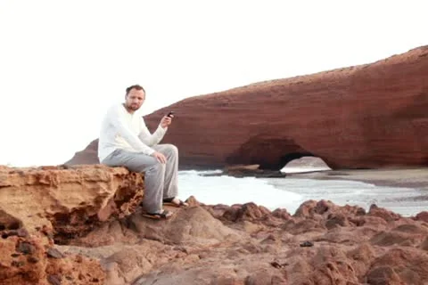 Man using cellphone on the rocks, Legzira beach Stockbeeldmateriaal 10891760