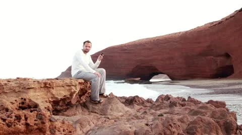 Man using cellphone on the rocks, Legzira beach 스톡 동영상 10891990