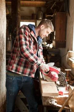 A man using an circular saw on a plank in a workshop Stock Photos
