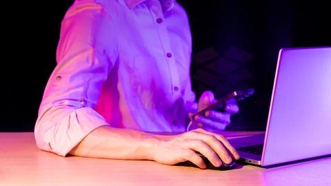 Man using computer and phone with holographic box icon in purple light Stock Photos