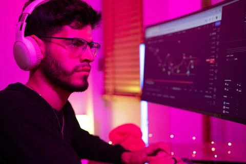 Man using computer in a dimly lit room with purple lighting focused on stoc.. 스톡 사진