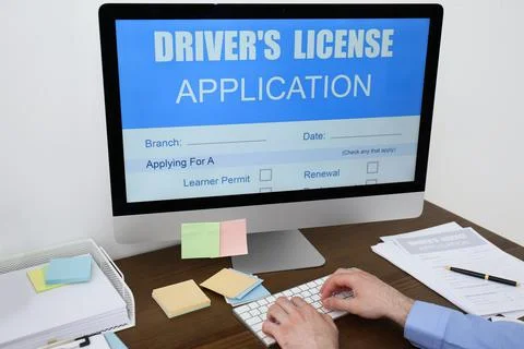 Man using computer to fill driver's license application form at table in offi Stock Photos