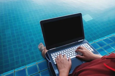 A man using computer laptop, at poolside with dipping legs in the water Stock Photos