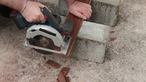 Man using a cordless circular saw to cut a piece of wood from demolition. Video stock 321890660