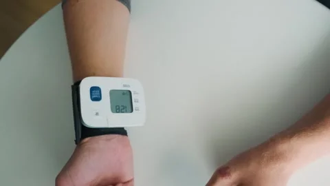 Man using digital wrist blood pressure monitor for measuring blood pressure and Stock Footage 315860312