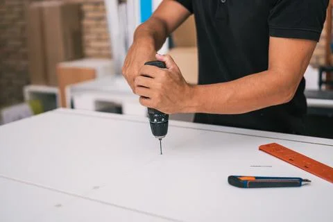 Man using a drill to make a small hole in a white surface in a workshop Stock Photos