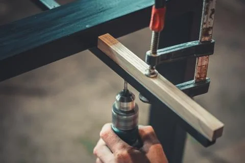 Man using the drill makes a hole in wood and iron strap. The process of makin Stock Photos