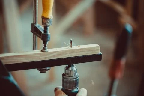 Man using the drill makes a hole in wood and iron strap. The process of makin Stock Photos