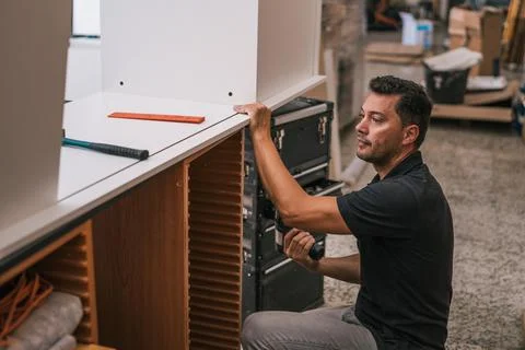 Man using a drill to put together two pieces of furniture in a workshop Stock Photos