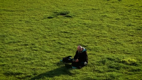 Man using drone remote controller while working on grass with laptop. Freelancer Stock Footage 311815168