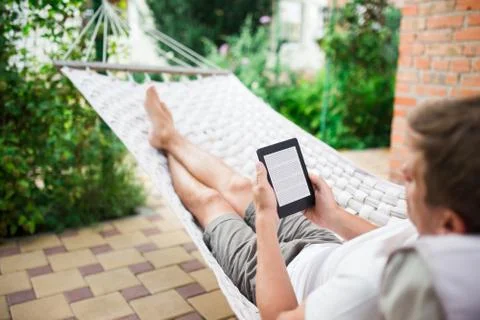 Man using e-book with lorem ipsum text on screen while relaxing in a hammock. Stock Photos