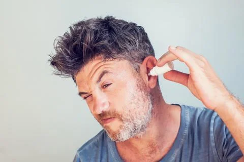 Man using ear drops on gray background Stock Photos