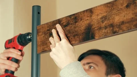 Man using electric drill to attach wooden board to coat rack. Male assembling Stock Footage 309397992