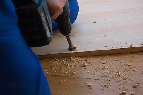 A man using an electric hand drill for work with a board, sawdust all around Stock Photos