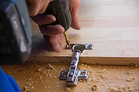 A man using an electric hand drill for work with a board, sawdust all around Stock Photos