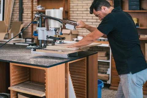 Man using an electric machine to cut a wooden panel in a workshop. Stock Photos