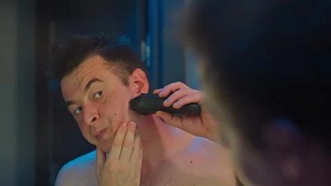 Man Using Electric Razor While Looking in the Bathroom Mirror Stock Footage 289406066