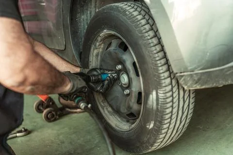 Man using an electric screwdriver to remove a wheel in a garage Stock Photos