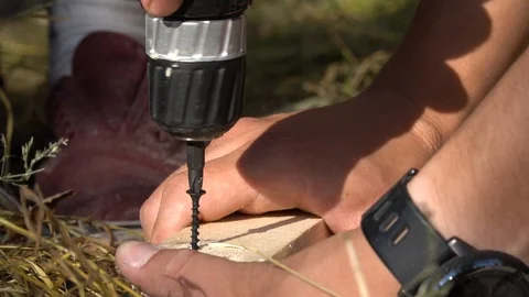 Man using an electric screwdriver on wood, on the floor with grass. Vidéo 110256761
