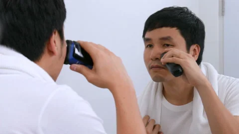 Man using electric shave to shaving his face in the bathroom mirror Stock Footage 153697533