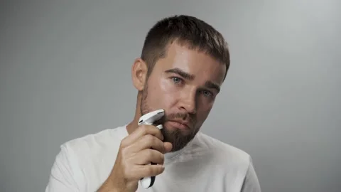 Man is using electric trimmer for beard shaving against gray background Stock Footage 233518472