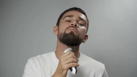 Man is using electric trimmer for beard shaving against gray background Vídeo Stock 233518643