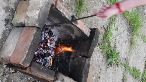 Man using fire iron to mix firewood inside rustic fireplace outdoors with smoke Stock Footage 154458732