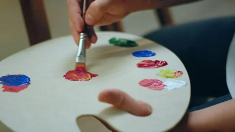A man is using a flat brush to mix two colours on a palette and paint onto a 스톡 동영상 229695716