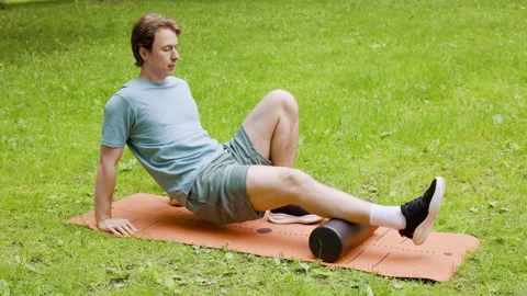 Man using a foam roller for myofascial release on a mat outdoors. Perfect self-m Stock Footage 342053567