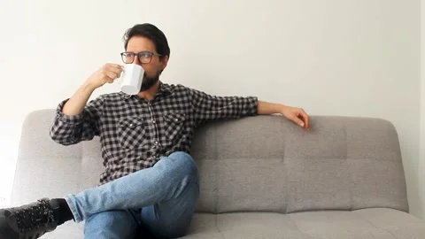 Man using glasses sitting on the left side of a couch drinking a beverage Stock Footage 340583379