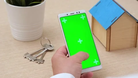 Man using green screen phone in vertical position near house model and keys Stock Footage 274343641