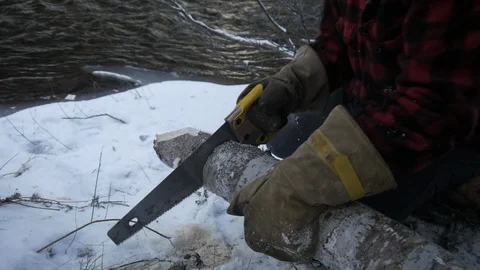 Man using hand saw to cut end of log in winter by stream Stock Footage 121219530