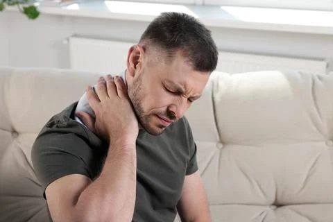 Man using heating pad on sofa at home 库存照片