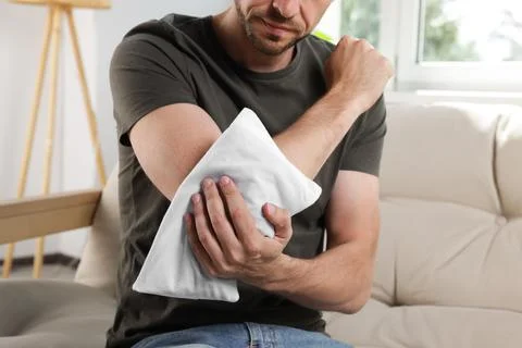 Man using heating pad on sofa at home, closeup 库存照片
