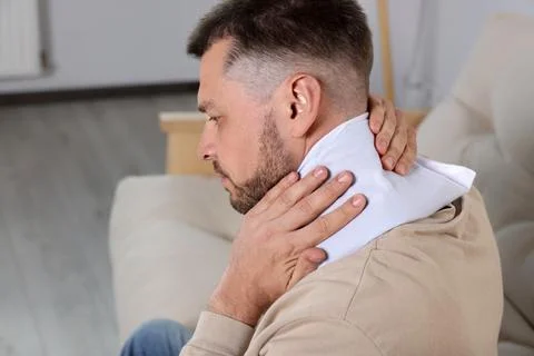 Man using heating pad on sofa at home 스톡 사진