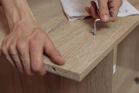 Man using hex key and screwing bolt into wooden plank of table Stock Photos
