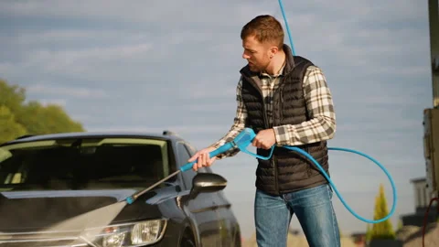 A man using a high-pressure water hose to clean his car's surface Stock Footage 297129544