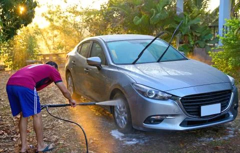 Man using high pressure water cleaning grey car during morning with sun ray Stock Photos