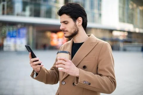 Man using his cellphone and holding a cup of coffee while walking in a city Fotos de archivo