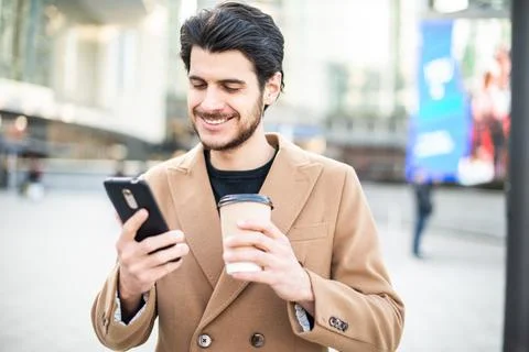 Man using his cellphone and holding a cup of coffee while walking in a city Stockfoto's