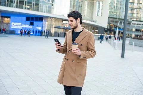 Man using his cellphone and holding a cup of coffee while walking in a city Stock Photos