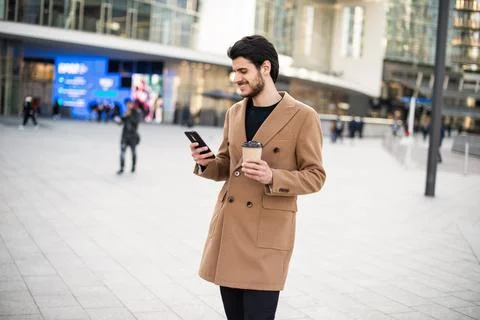 Man using his cellphone and holding a cup of coffee while walking in a city Foto stock