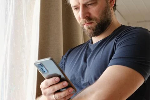 Man using his cellphone. Handsome guy use mobile phone at home. Male browses Stock Photos