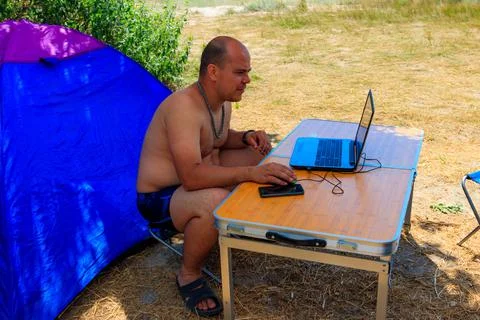 Man using his laptop sitting at a folding picnic table in a camping Stock Photos