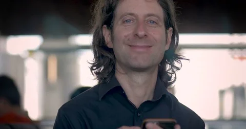 Man using his mobile phone looks up and smiles inside airport terminal Video stock 84630218