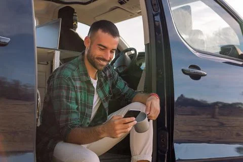 Man using his mobile phone sitting on his camper Stock Photos